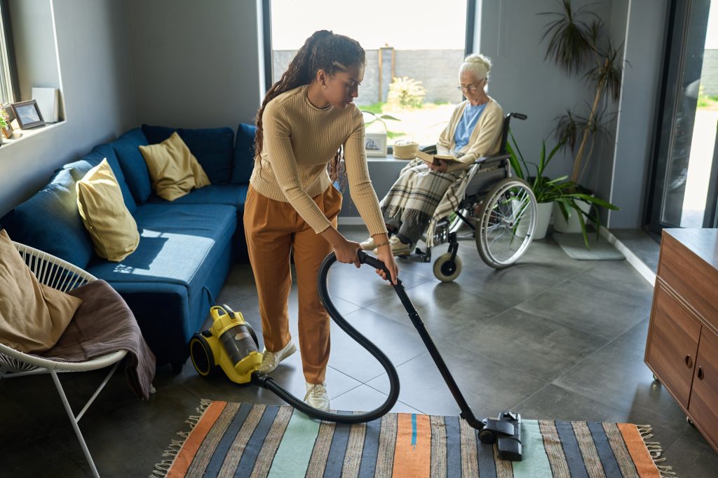 Youthful,Girl,With,Vacuum,Cleaner,Helping,Her,Grandmother,With,Disability